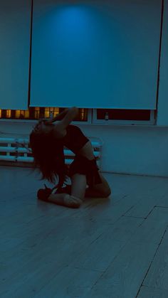 a woman sitting on the floor in front of a blue light with her hands behind her head