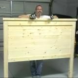 a man standing behind a wooden sign in a garage with his hands on the back of it