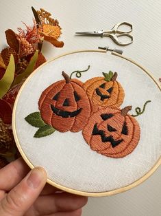 a hand holding a hoop with three pumpkins on it and some scissors next to it