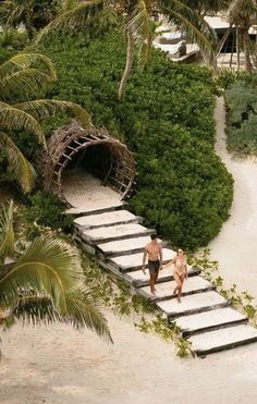 two people are walking up some stairs on the beach in front of trees and bushes