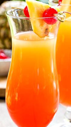 two glasses filled with orange juice and garnished with pineapple on the rim