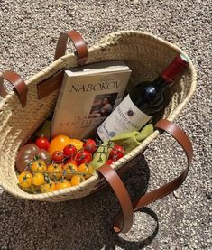 a basket filled with assorted fruits and vegetables next to a bottle of wine on the ground