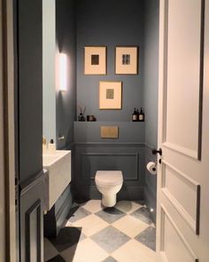 a white toilet sitting inside of a bathroom next to a sink and mirror with pictures on the wall