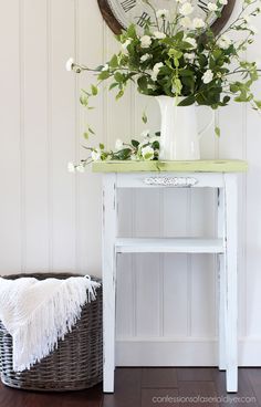 a white table with flowers and a clock on the wall behind it, in front of a wicker basket