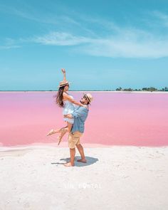 a man and woman are standing on the beach with their arms in the air while holding each other