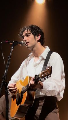 a young man holding a guitar while standing in front of a microphone