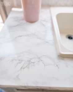 a marble counter top next to a sink with a pink cup on it and a faucet in the background