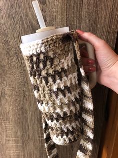 a woman is holding a coffee cup in a cozy crocheted mug holder with a straw sticking out of it