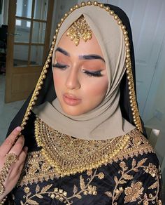 a woman wearing a hijab and headpiece with gold jewelry on her face