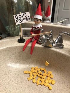 an elf is sitting in the sink with some fish crackers next to it and a sign that says gone fishing