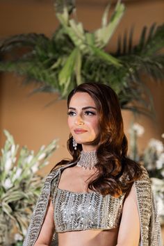 a beautiful woman in a silver and gold outfit standing next to a potted plant