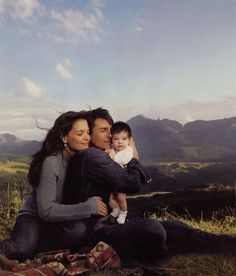 a man, woman and child are sitting in the grass with mountains in the background