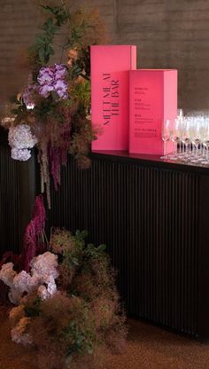 there are many wine glasses sitting on the bar with flowers and bottles in front of them