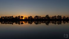 the sun is setting over some trees on the water's edge, and it looks to be reflecting in the water