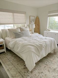 a white bed sitting next to two windows in a bedroom on top of a rug