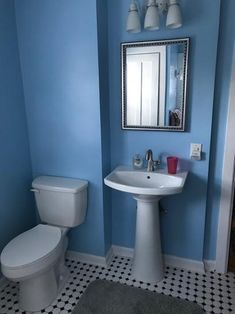 a white toilet sitting next to a sink under a mirror in a blue walled bathroom