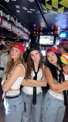 three young women standing next to each other in front of a bar with neon signs on the ceiling