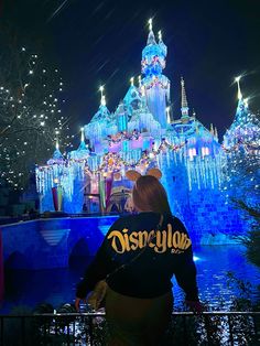 a woman standing in front of a castle at night with lights on it's walls