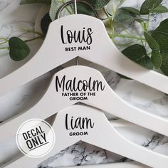 three white wooden hangers with black lettering on them and green leaves in the background