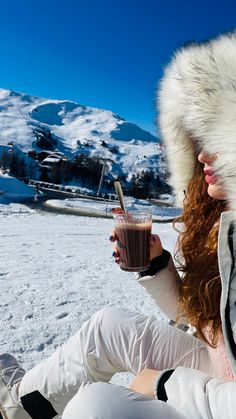 a woman sitting in the snow holding a drink