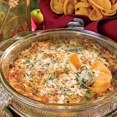 a casserole with cheese and spinach in a bowl next to some chips