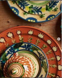 an orange and blue plate sitting on top of a wooden table next to other plates