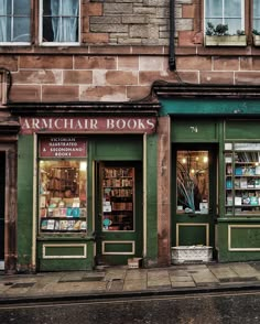 an old brick building with green shutters and books on the front, next to a sidewalk