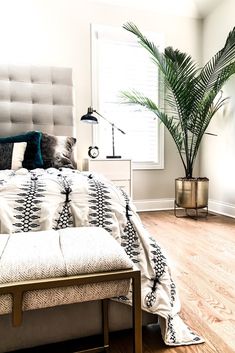 a bedroom with a large bed and a plant in the corner on the side of the bed