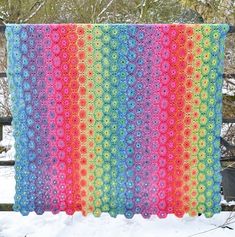 a multicolored crocheted blanket is hanging on a fence in the snow