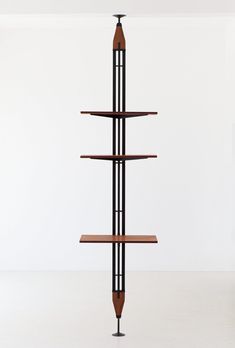 a tall wooden shelf sitting on top of a white floor next to a black metal pole