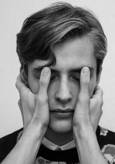 black and white photograph of a young man holding his hands to his face while looking at the camera