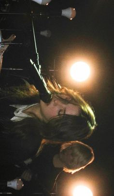 a woman with long hair standing in front of a microphone on stage at night time