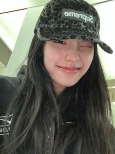 a girl with long hair wearing a hat and smiling at the camera while holding her phone up to her face