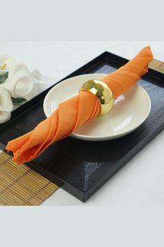 an orange napkin sits on a white plate next to a gold ball and bamboo mat