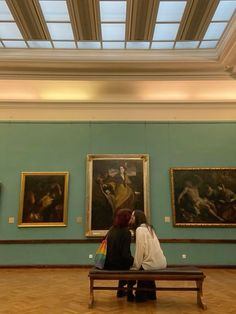 two women sitting on a bench in front of paintings