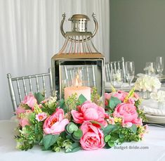 a table topped with a vase filled with pink flowers and a lit candle on top of it