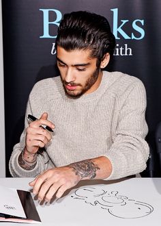 a man sitting at a table with a cell phone in his hand and writing on the paper