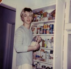 a young man is standing in front of an open refrigerator holding a jar and looking at the camera