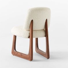 an upholstered chair with wooden legs and a white sheepskin seat cover on the back