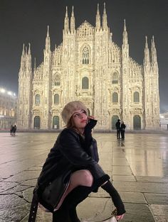 a woman sitting on the ground in front of a large building with tall spires