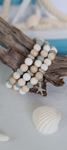 a bracelet made out of beads and seashells sits on a driftwood branch