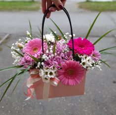 a hand holding a pink and white flower arrangement in a brown paper bag on the street