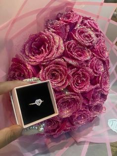 a person holding a ring in front of a bouquet of flowers with pink roses on it