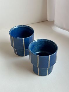 two blue cups sitting next to each other on a white counter top in front of a window