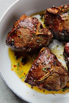 three pieces of cooked meat in a white bowl with sauce and garnish on the side