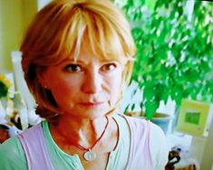 a woman with blonde hair wearing a necklace and looking at the camera while standing in front of a window