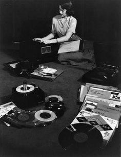 a woman sitting on the floor surrounded by old record players and other items that have been placed around her