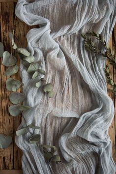 the fabric has been draped over and is next to eucalyptus leaves on a wooden table