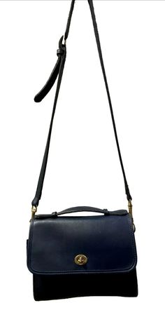 This beautiful vintage Coach Court Bag 9870 is a stylish addition to any wardrobe. Made of dark blue leather with gold hardware, it features a turn lock closure and a shoulder strap with a drop of 23-27 inches. The size of this bag is medium, with a width of 9 inches, a height of 9 inches, and a depth of 3 inches. The interior is classic vintage coach, which is unlined. So, it's blue leather inside and has one main compartment and an interior zipped pocket. There is one exterior slip pocket on the back. The bag has a square shape and a strap accent, making it a unique and fashionable accessory. Perfect for everyday use, this shoulder bag from the Coach Court collection is a must-have. Gently Pre-Owned. Remarkable condition given its age. Some minimal light wear and slight surface scratches Office Shoulder Bag Satchel With Brass Hardware, Office Satchel With Top Handle And Brass Hardware, Blue Office Bag With Hasp Closure, Evening Satchel With Brass Hardware, Shoulder Bag Shape, Classic Office Shoulder Bag With Brass Hardware, Evening Satchel With Brass Hardware, Office Crossbody Bag With Brass Hardware, Formal Crossbody Flap Bag With Hasp Closure, Crossbody Bags With Brass Hardware