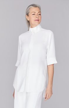 A classic mandarin collar tunic featuring two deep pleats at the center back for movement and comfort. This tunic has elbow length sleeves and buttons down the front. Modern White Blouse With Concealed Placket, Elegant Blouse With Shirttail Hem And Placket, Elegant Blouse With Placket And Shirttail Hem, Stand Collar Shirt With Placket For Workwear, Workwear Shirt With Stand Collar And Placket, Elegant Daywear Tunic, Classic Stand Collar Top For Work, Modern White Blouse With Placket, Classic Stand Collar Tops For Work